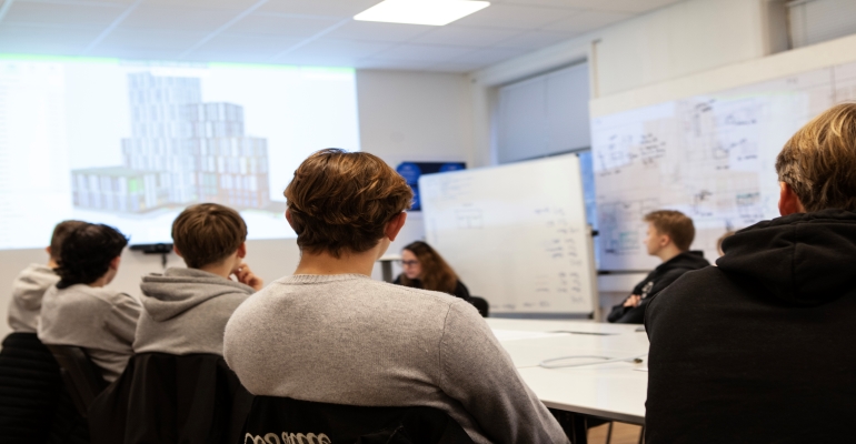 elever fotat bakifrån sittandes vid mötesbord.